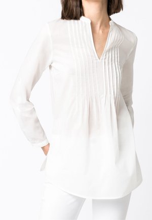 Blouse blanche à manches longues avec un détail plissé à l'avant et un décolleté en V. Fabriquée en tissu léger, elle présente un ourlet incurvé et un minimalisme dans les détails.