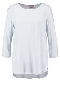 Blusa azzurro chiaro a maniche lunghe con scollatura rotonda, texture morbida, spacchi laterali e orlo posteriore leggermente più lungo. Etichetta visibile sul collo.