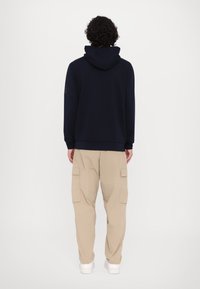 Felpa con cappuccio blu navy dal taglio rilassato, abbinata a pantaloni cargo beige con tasche laterali, entrambi realizzati in tessuto morbido.