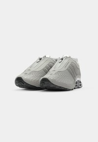 Zapatillas deportivas grises con parte superior texturizada, cierre de cremallera y suela acolchada. Presentan un diseño aerodinámico y detalles en patrón en los laterales.