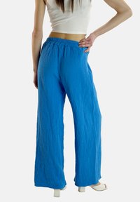 Pantaloni ampi plissettati blu con vita elasticizzata, tessuto texturizzato e vestibilità rilassata, abbinati a tacchi bianchi spessi.