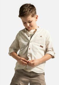 Jasno beżowa bawełniana koszula z kołnierzykiem typu button-down, długimi rękawami podwiniętymi do góry. Posiada przednią kieszeń oraz drewniane akcenty guzików.