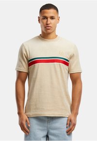 Camiseta beige de manga corta, con un diseño de rayas horizontales en rojo, verde y azul a lo largo del pecho. Pequeño logo en el lado izquierdo.