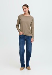 Beige langermet topp med rund hals, kombinert med rette blå jeans og beige slip-on sko. Glatt stoff og avslappet passform.
