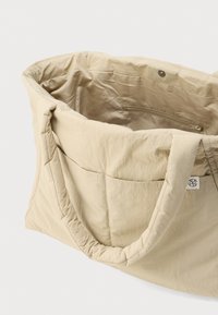 Μπεζ τσάντα τύπου tote με επένδυση, φαρδιές λαβές, δύο εξωτερικές τσέπες, εσωτερική τσέπη με φερμουάρ και κλείσιμο με κουμπί πατιλέτα.