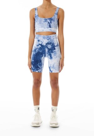 Sujeción deportiva de estilo tie-dye en tonos azules y pantalones cortos de talle alto a juego, diseño ajustado, material suave, textura lisa, con zapatillas y calcetines blancos.