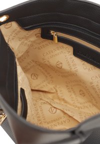 Interno della borsa in pelle nera caratterizzato da un tessuto beige con un motivo ripetuto del logo "Café Noir" e una tasca con zip con hardware dorato.