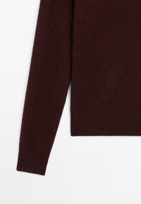 Bordowy sweter dzianinowy o prostokątnym kroju, z długimi rękawami i prążkowanym wykończeniem. Miękka tekstura, prosty design, bez widocznych wzorów czy elementów metalowych.