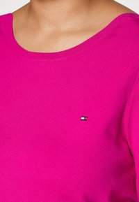 Top de punto fucsia con escote redondo y mangas cortas, que presenta un pequeño logo tricromático bordado en el pecho.