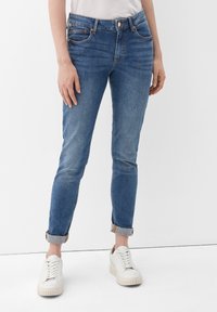 Blå denimjeans med en figurnära design, medelhög midja, upprullade ärmslut och detaljer i koppar. Bärs med vita sneakers.