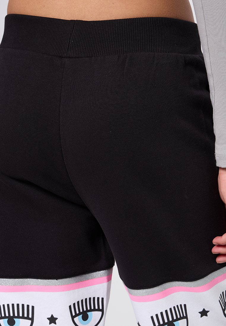 Schwarze Jogginghosen mit dehnbarem Bund, die mit einem bunten Grafikdruck versehen sind, der große blaue Augen und Sterne an den Unterschenkeln zeigt, mit einem glänzenden silbernen Akzent.