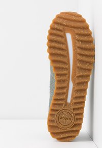 Harmaat lenkkarit, joissa on teksturoidut päälliset, kuminen pohja, jossa on syvät urat, sekä ympyrälogo, johon on merkitty "WODEN" pohjassa.