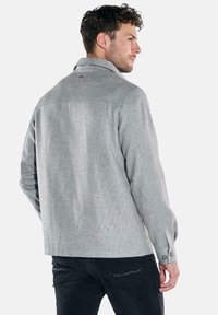 Gray textured shirt with a collar and buttoned cuffs, featuring a straight cut and subtle pattern. Worn with dark jeans.