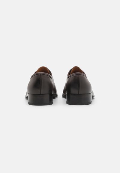 Pantofi din piele maro închis, cu o textură netedă, vârf rotund, cusături contrastante și un toc negru de profil redus. Detalii de marcă distinctive pe interior.