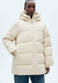 Beige pufferjack met een capuchon, met een rits aan de voorkant, doorgestikt ontwerp en geribbelde manchetten. Soepele textuur, knielange stijl.