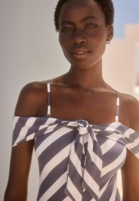 Maillot de bain décolleté en rayures bleu marine et blanches, avec un détail avant noué et des bretelles réglables fines. Matière douce et lisse.
