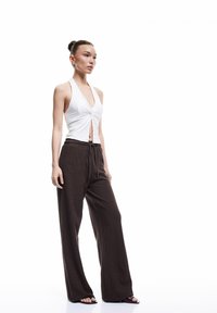 Witte geknoopte tanktop gecombineerd met losse bruine textuurbroek. Model draagt eenvoudige sandalen met een overall strakke silhoeët.