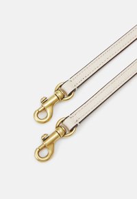 Skórzany pasek w kremowym kolorze z złotymi okuciami, wyposażony w dwa metalowe klipsy i kontrastujące ciemne krawędzie. Gładka faktura i smukły design.