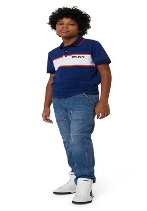 Polo bleu marine avec des rayures horizontales rouges et blanches, jeans en denim, et baskets montantes blanches avec la marque DKNY.