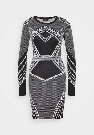 Robe moulante à manches longues en noir et blanc avec des motifs géométriques et tribaux, silhouette ajustée et encolure ronde.