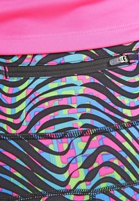 Haut de sport rose vif associé à des leggings de compression noirs à motifs avec des designs géométriques bleus, roses et verts, et une poche zippée.