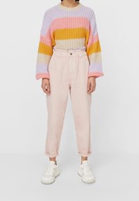 Mångfärgad stickad tröja med horisontella ränder i lila, rosa, gult och krämfärgat. Kombinerad med ljusrosa högmidjade byxor och vita sneakers.