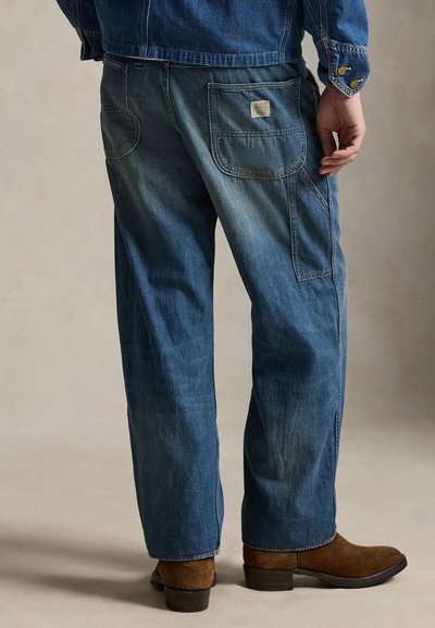 Μπλε παντελόνι από τζιν με χαλαρή εφαρμογή, με πίσω τσέπες και διακριτική ξεθώριαση. Συνδυασμένο με καφέ καστόρινες μπότες.