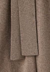 Gros plan sur un tissu tricoté beige doux avec des panneaux verticaux superposés et un motif tricoté texturé.