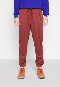 Maroon sweatpants with elastic cuffs and drawstring waist, featuring a black Nike logo. Paired with orange lace-up sneakers.