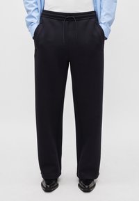 Navyblaue Jogginghose aus weichem Material mit einem Kordelzugbund, seitlichen Taschen und lockerer Passform. Getragen mit einem hellblauen gestreiften Hemd.