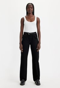 Mustad laia säärega kõrge vöökohaga teksad, koos valge soonelise toppiga. Punutud must vöö ja mustad paeltega kingad. Puhtad, minimalistliku disainiga.