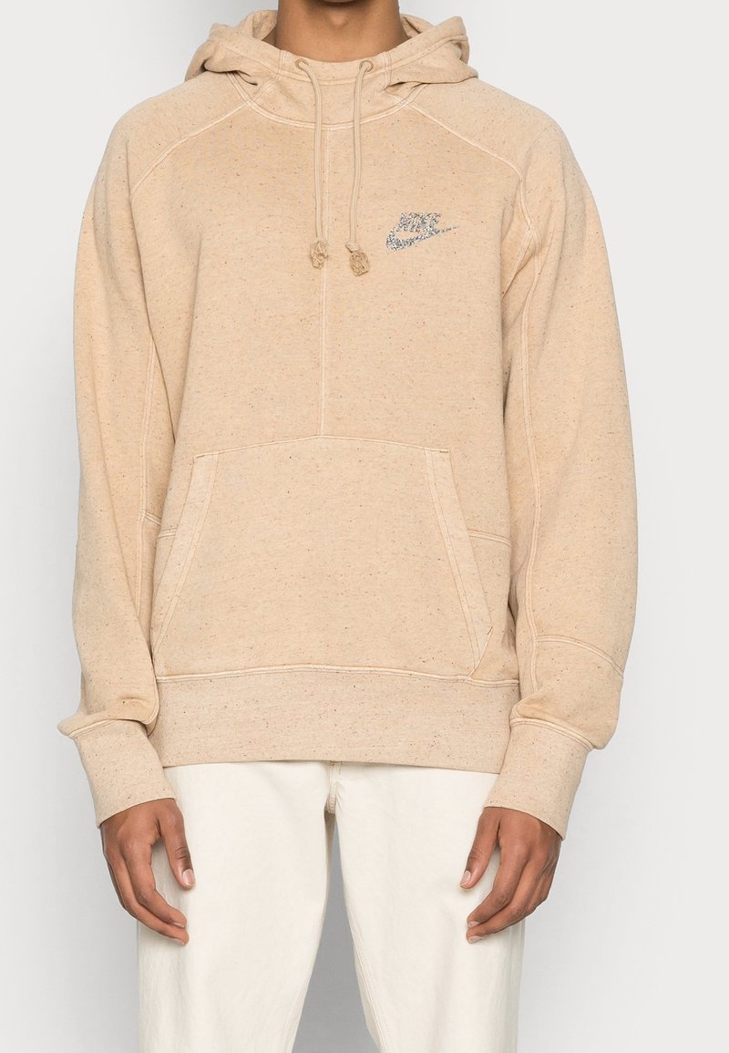 Beige cotton hoodie featuring a front pocket, drawstring hood, and a small embroidered logo in blue on the left chest. Soft texture.