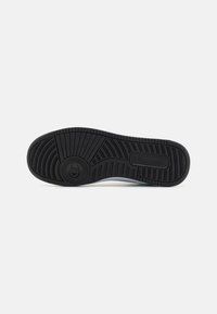 Suola in gomma nera per sneaker con motivo di battistrada testurizzato e dettaglio del logo circolare, caratterizzata da un design curvo e bordi leggermente alzati.