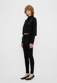 Schwarzes, tailliertes Shirt mit gestickten Details, kombiniert mit schmalen schwarzen Hosen und spitzen schwarzen Absatzschuhen. Glatter Stoff, perfekter Sitz, minimales Design.