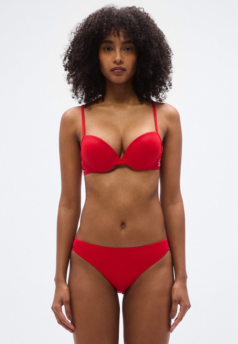 Σετ κόκκινου μπικίνι με επενδυμένο σουτιέν και ρυθμιζόμενους ιμάντες, συνοδευόμενο από αντίστοιχα σλιπ χαμηλής μέσης. Ομαλό, ελαστικό υλικό με αδιάκοπη σχεδίαση.