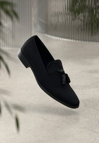 Pantofi loafers negri cu un superior din material neted, vârf ascuțit și ciucuri decorativi. Au un toc mic, rotund și un design minimalistic.
