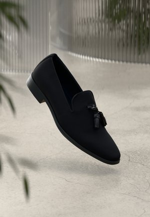 Schwarze Slipper mit einem glatten Obermaterial, spitzem Zeh und dekorativen Quasten. Verfügt über einen niedrigen, abgerundeten Absatz und ein minimalistisches Design.