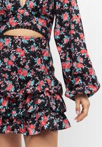 Černý květinový crop top a sukně, zdobené volány, dlouhými zvonovými rukávy a vzorem červených a tyrkysových květin na tmavém pozadí.