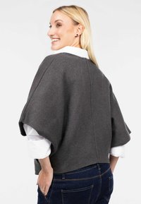 Pelēks adīts pončo ar plašām piedurknēm, ar taisnu apakšmali un šuvumu bez muguras daļā. Valdāms pār baltu krekla apkakli un zilām džinsiem.