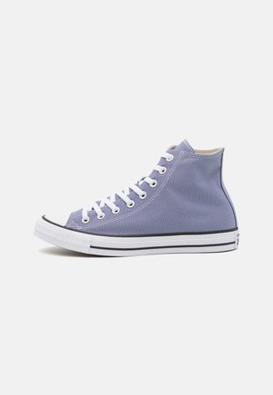 Hoog model canvas sneaker in lichtpaars met witte veters en een rubberen zool met zwarte streep, gezien van opzij op een witte achtergrond.