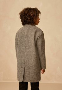 Houndstooth-frakke i grå og sort med rygslids, struktureret krave og lange ærmer. Materialet har et tekstureret vævdesign.