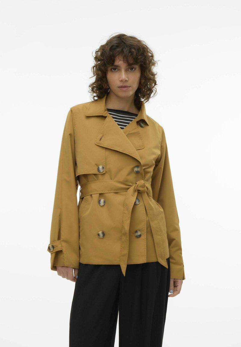Tan belted trenchcoat med dobbeltbrystet design, store knapper og klassisk krave. Sammen med en stribet top og brede sorte bukser.