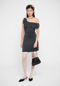 Vestido cinza de um ombro só com detalhes em renda, combinado com calções brancos de renda, meias transparentes, carteira preta e saltos agudos pretos.