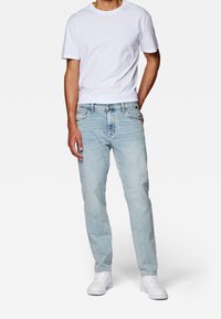 Vaqueros de denim azul claro con corte recto, que cuentan con bolsillos frontales, bolsillos traseros y una textura desgastada. Combinados con una camiseta blanca lisa.