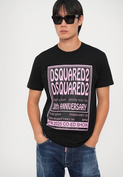 Camiseta negra con un gran texto gráfico rosa para el 30 aniversario de DSQUARED2. Se combina con jeans de mezclilla azules y gafas de sol negras.