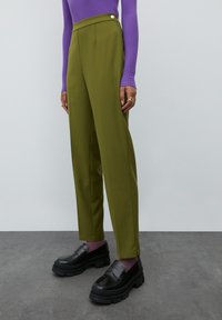 Olijfgroene pantalon met een hoge taille, zijknopdetails en een rechte pasvorm, gecombineerd met zwarte stevige loafers.