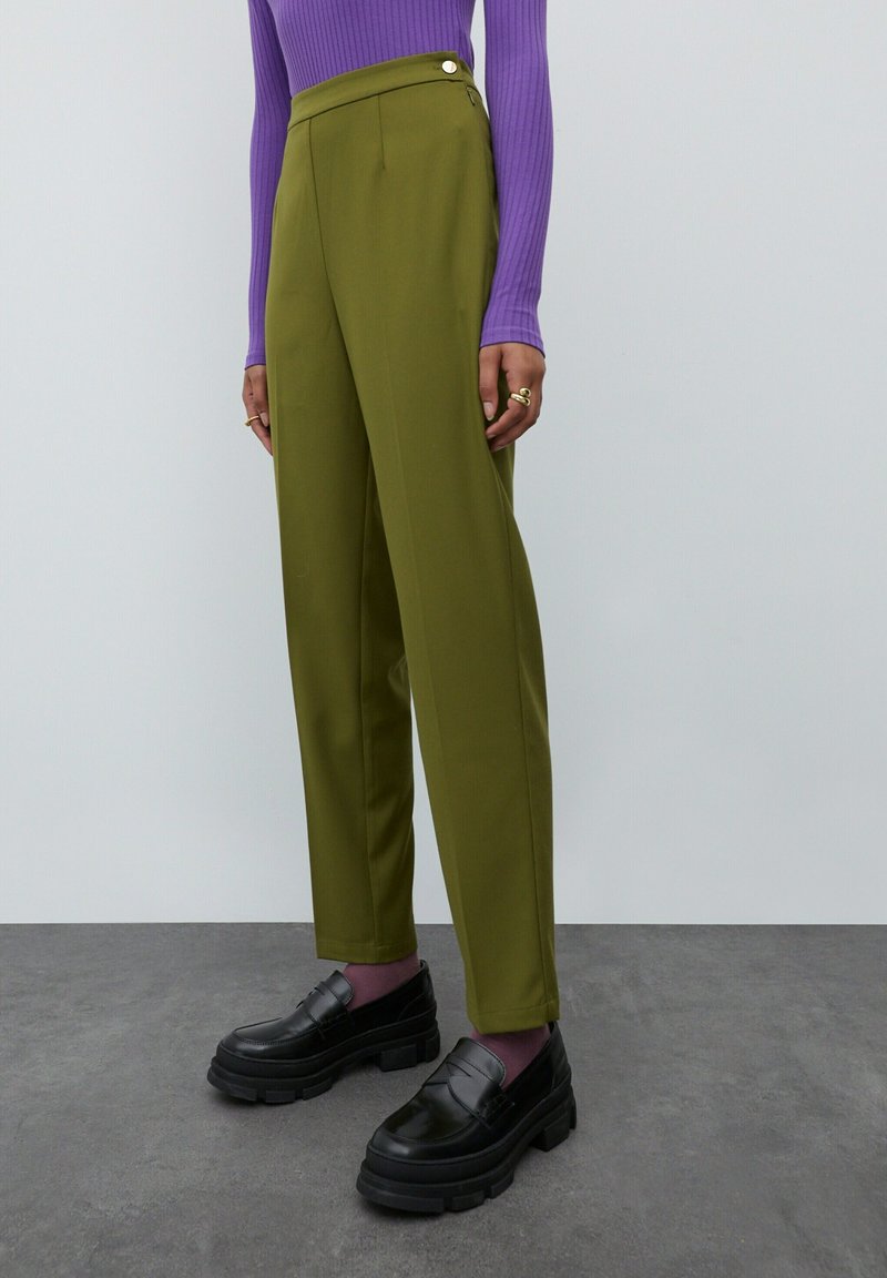 Olijfgroene pantalon met een hoge taille, zijknopdetails en een rechte pasvorm, gecombineerd met zwarte stevige loafers.