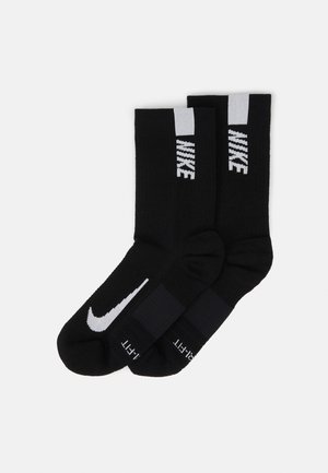 Black athletic socks featuring a white Nike logo and accent stripes at the top. Made of soft, textured fabric for comfort.