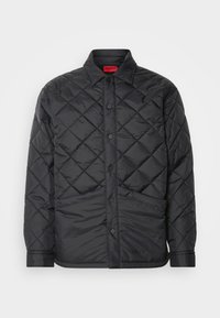 Veste matelassée noire avec col, boutons-pression à l'avant et poches latérales, arborant le logo de la marque en bas à droite.