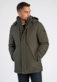 Oliven grøn quilted jakke med hætte, der har lynlåslukning, to forlommer og et logo-patch på ærmet. Glat tekstur.